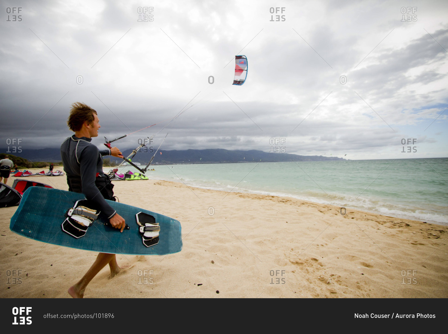 A kiteboarder prepares to hit the water on a beach on a cloudy summer day in Maui.