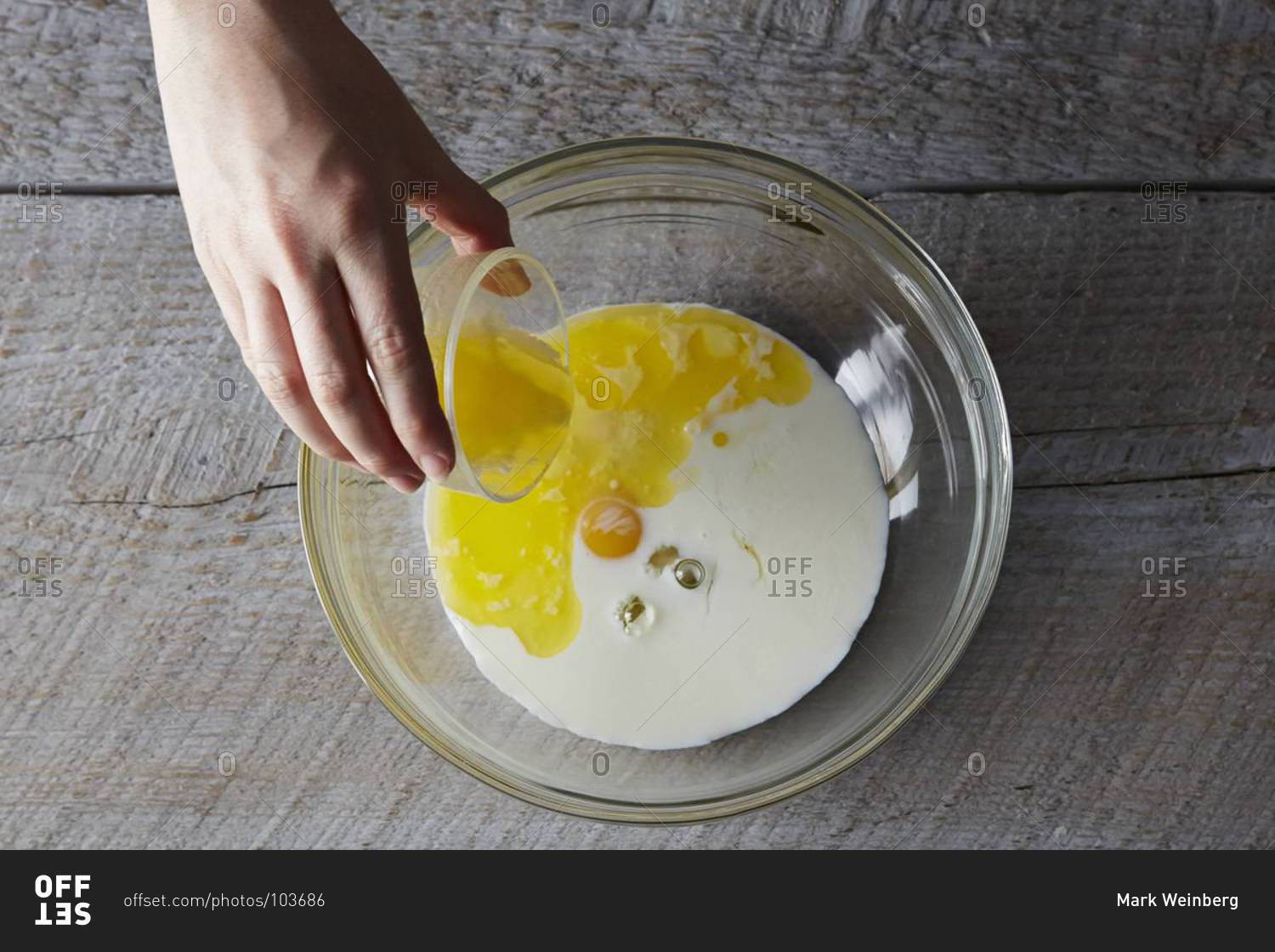 Pouring oil into a mixing bowl with egg and milk for pancakes stock