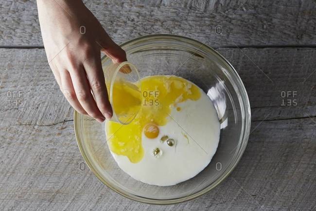 Pouring oil into a mixing bowl with egg and milk for pancakes stock ...