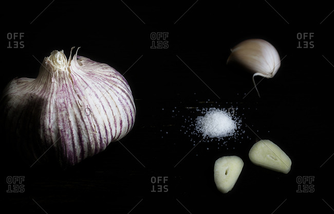 Garlic bulb, garlic clove, sliced garlic clove, and salt on a black background surface