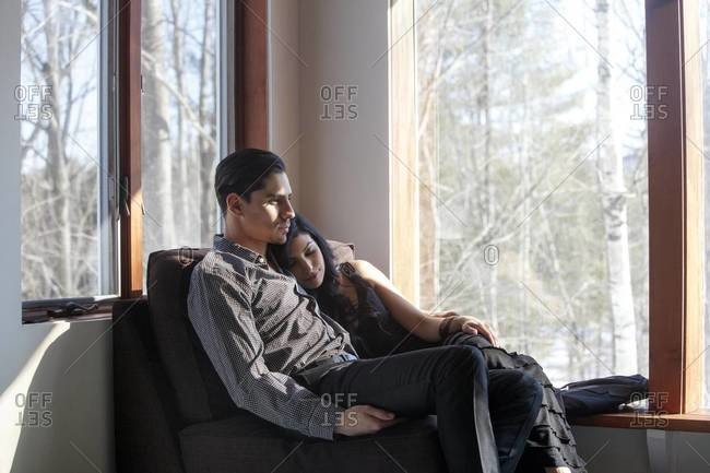 Young couple cuddling in chair by window