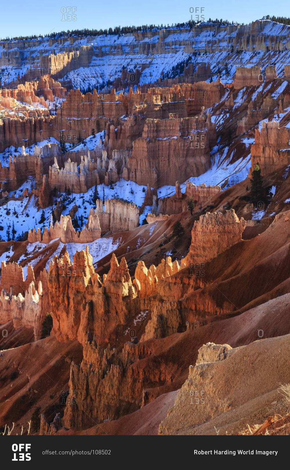 Hoodoos and snowy rim cliffs lit by strong late afternoon sun in winter, near Sunrise Point, Bryce Canyon National Park, Utah, United States of America, North America