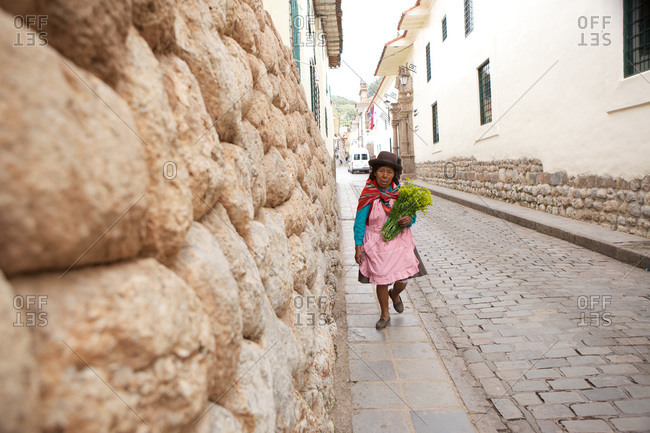Cusco, Peru - April 5, 2013: An elderly woman holding flower walking along a cobblestone street, Cusco, Peru.