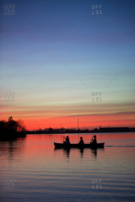 Silhouette of three woman paddling on the lake at sundown