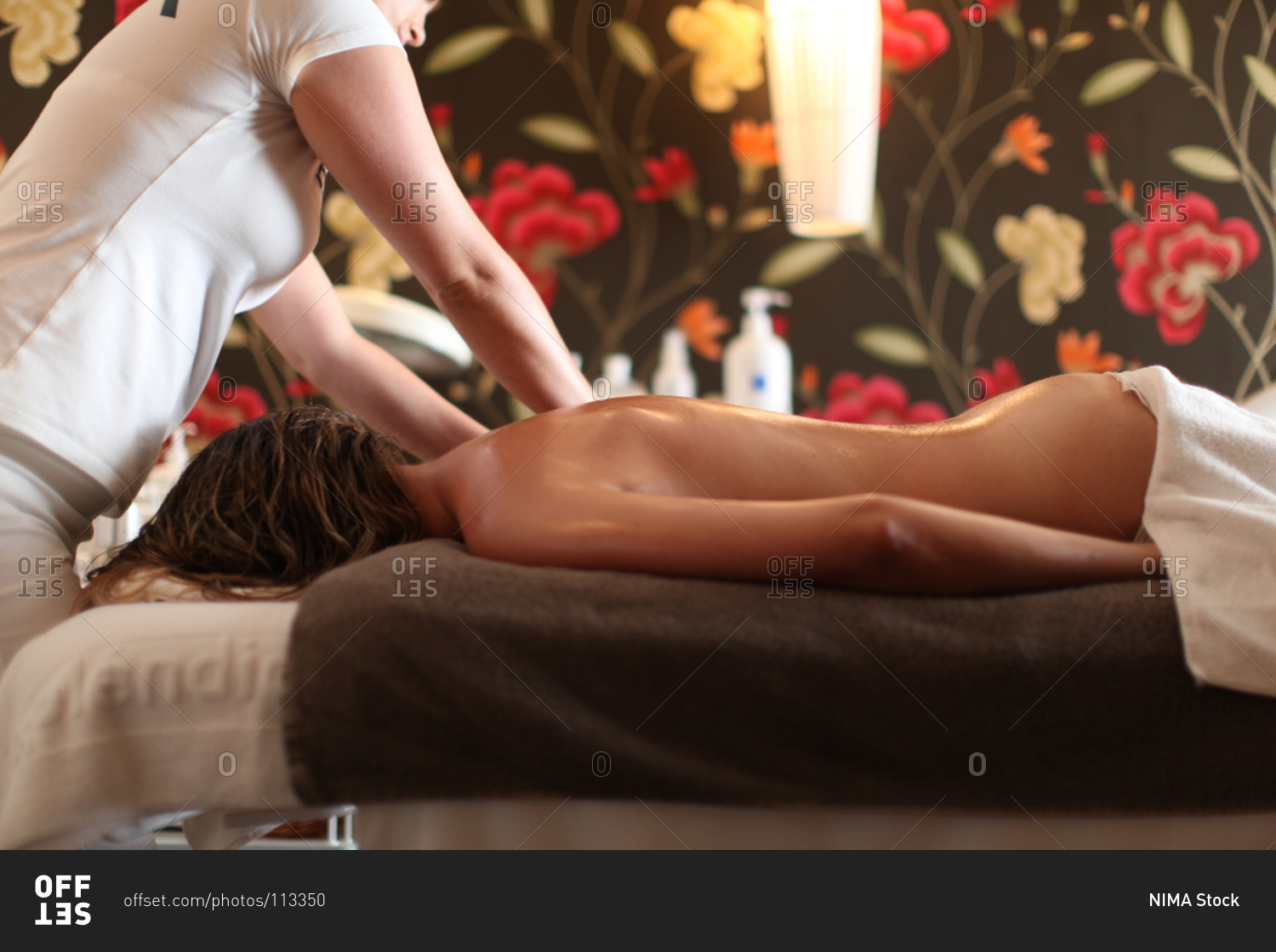 Naked woman receiving back massage from masseur at spa