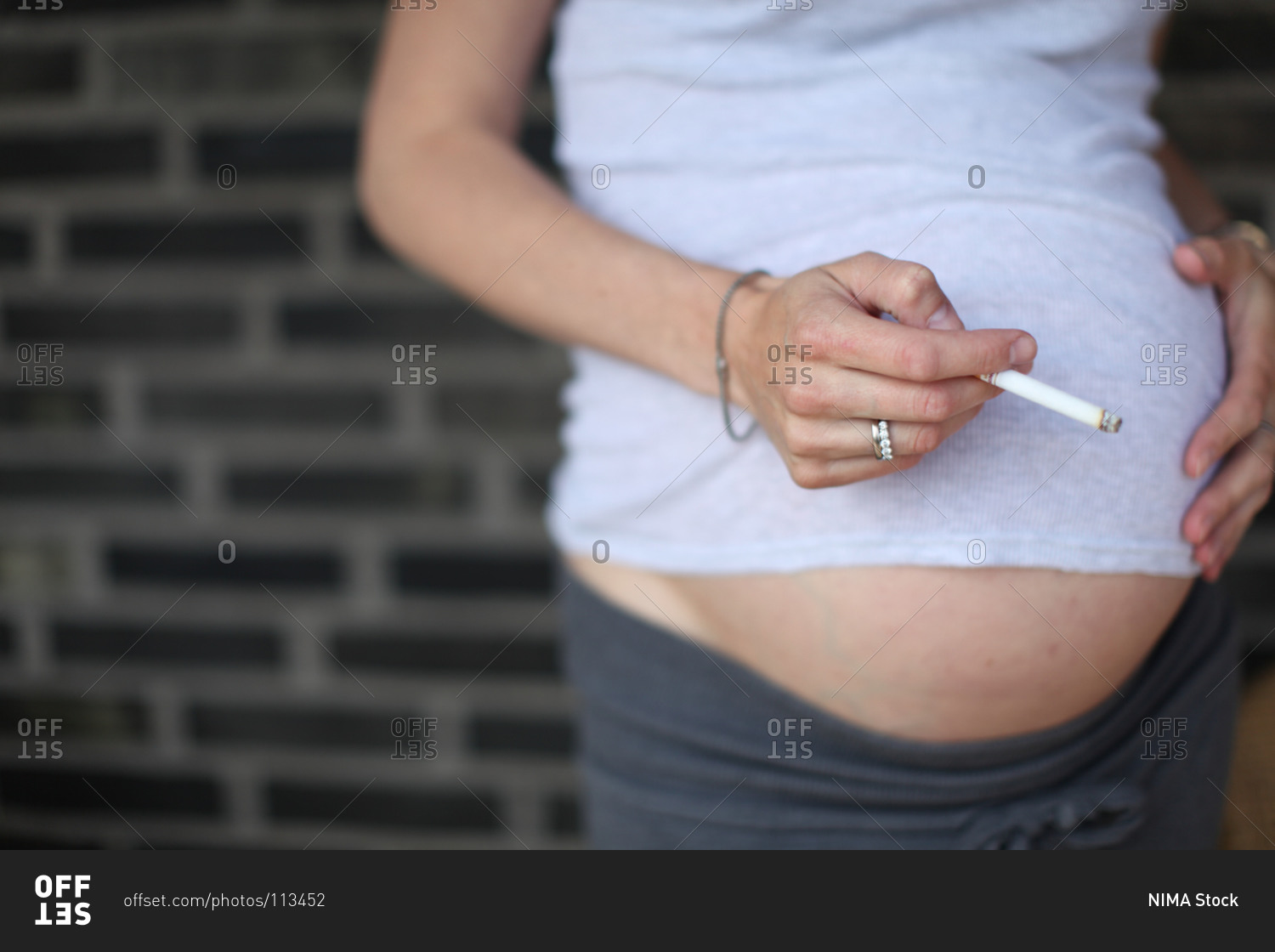 Woman touching her pregnant belly while smoking a cigarette stock photo