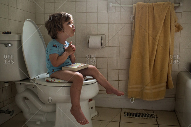 Toddler girl potty training holding toilet paper in bathroom Stock