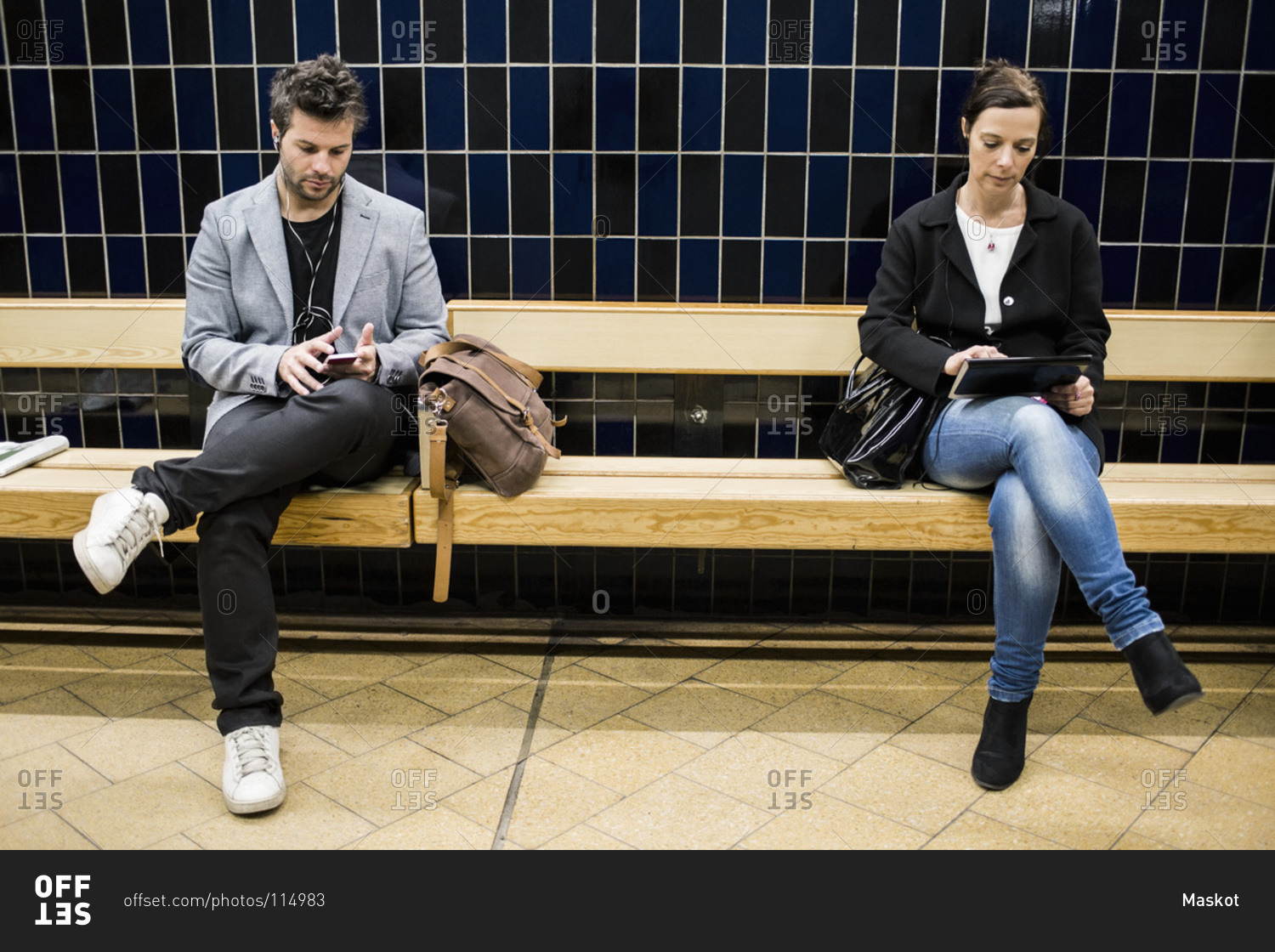 People using technologies on bench at subway station