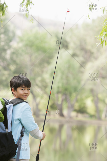 Boy carrying fishing pole by lake stock photo - OFFSET