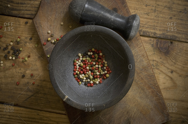 Mortar with dried green, red, white and black peppercorns on wood, elevated view