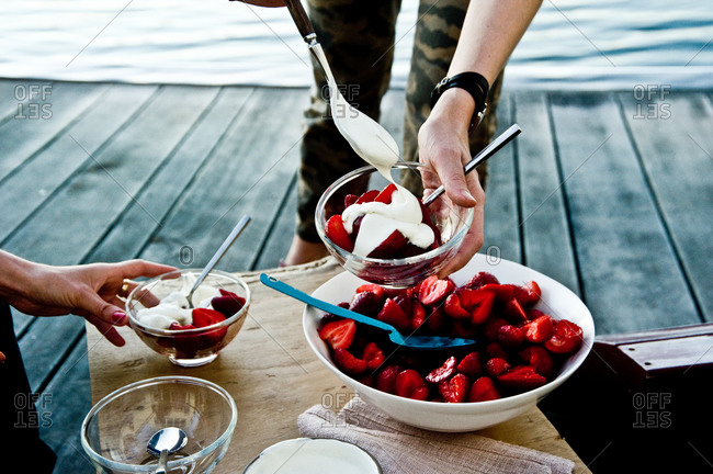 Person spooning chamomile cream over fresh strawberries
