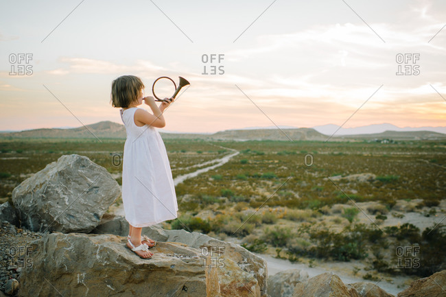 Young girl playing hunting horn on rock