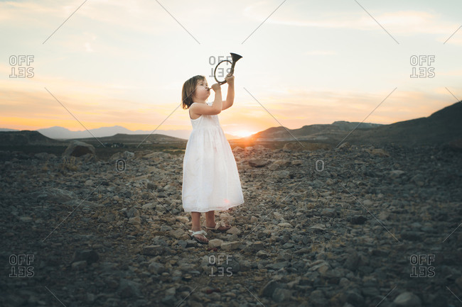 Young girl playing hunting horn at sunset