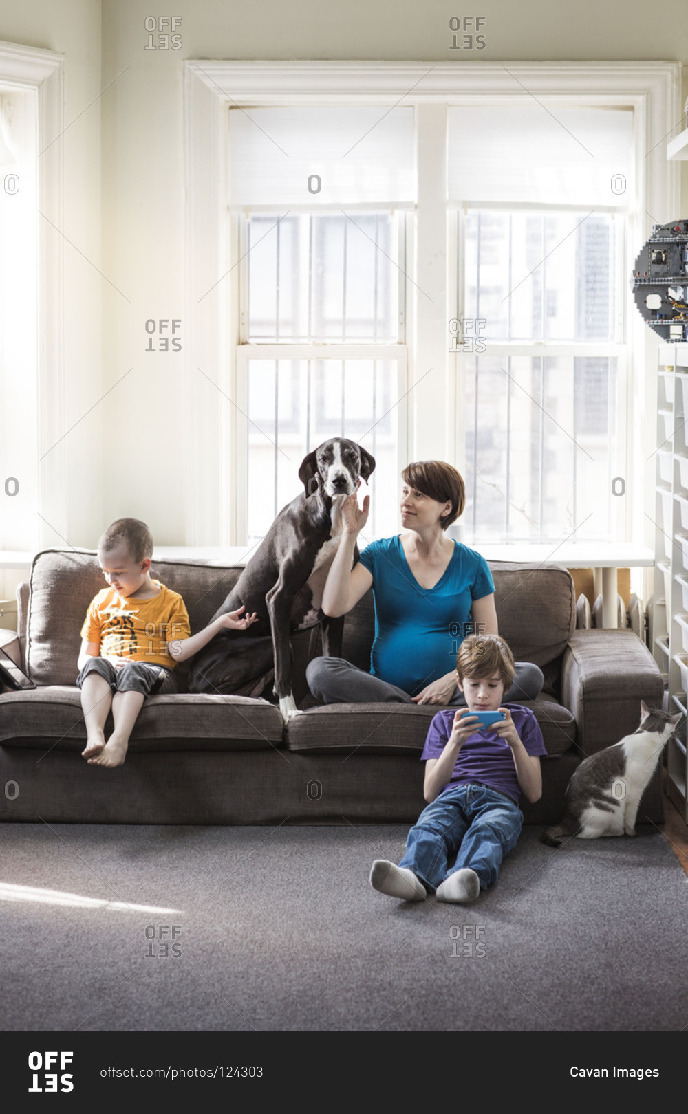 Pregnant mother, her two sons, and the cat and dog sit in the living room