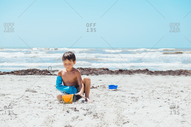 Boy with broken arm filling a bucket with sand on a beach