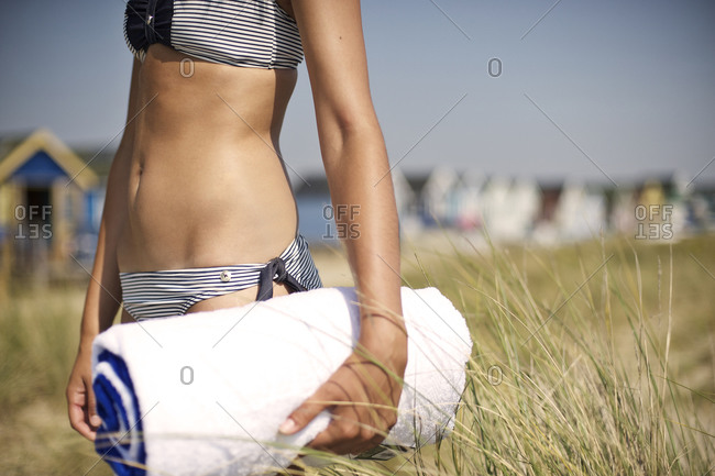 Mid section view of woman walking with folded beach towel