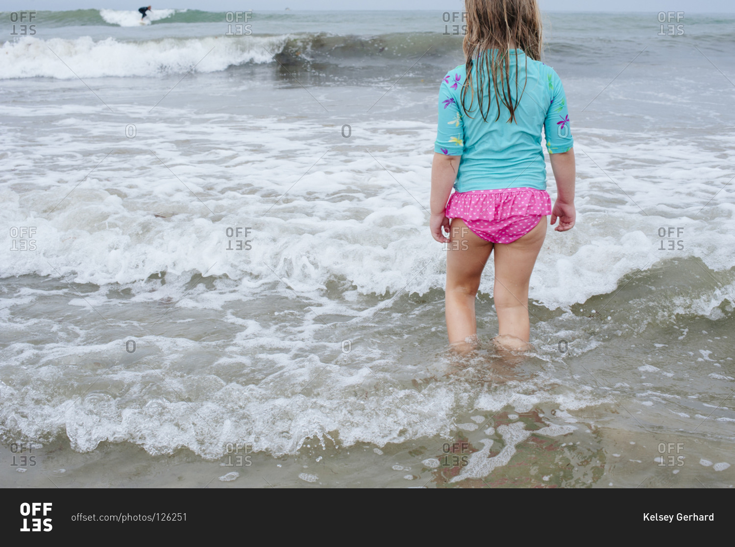 Back view of little girl in panties carrying blue swimming board while  walking on wet sand near sea stock photo - OFFSET