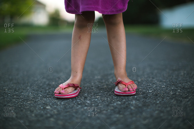 A little girl wearing mismatched flip flops stock photo - OFFSET