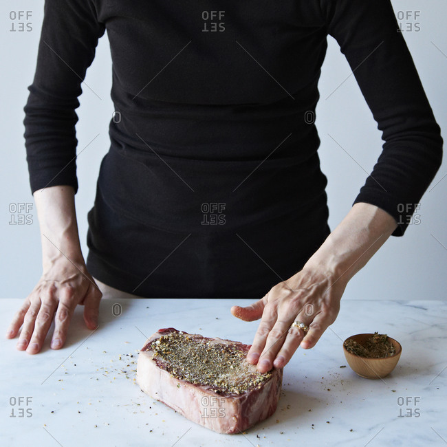 Woman seasoning a steak chop with coarse spice blend