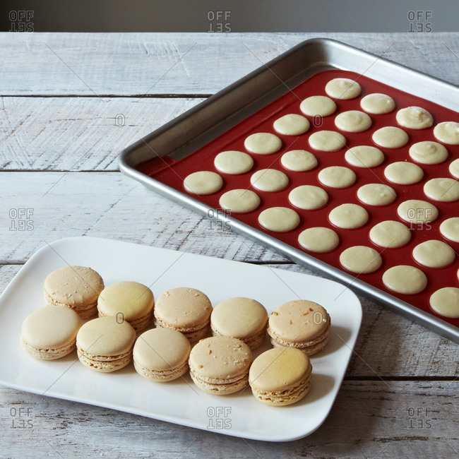 Freshly baked macaroons next to a tray of unbaked macaroons