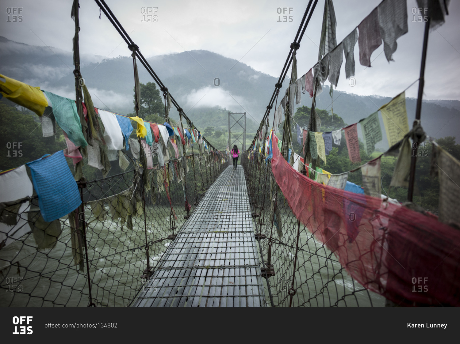 Woman crossing a suspension bridge covered in prayer flags, Bhutan