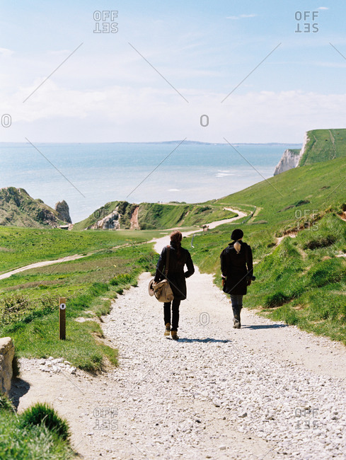 Two women walking on a coastal footpath along cliffs.