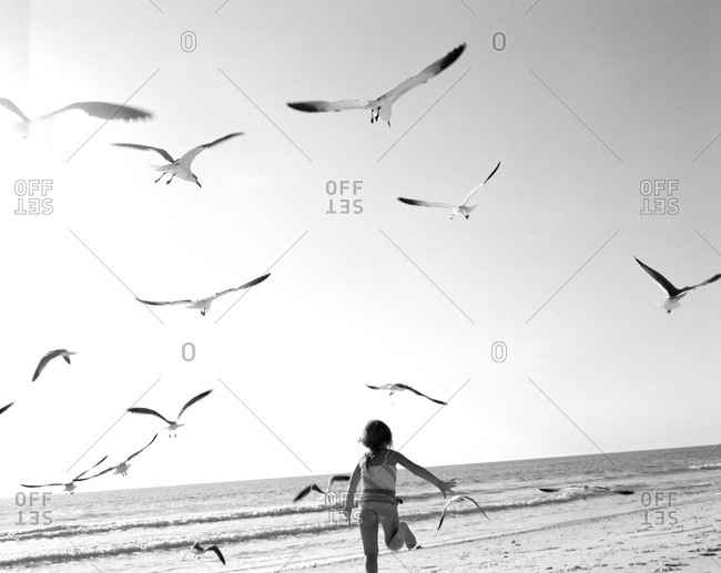 Young girl running between birds on a sandy beach