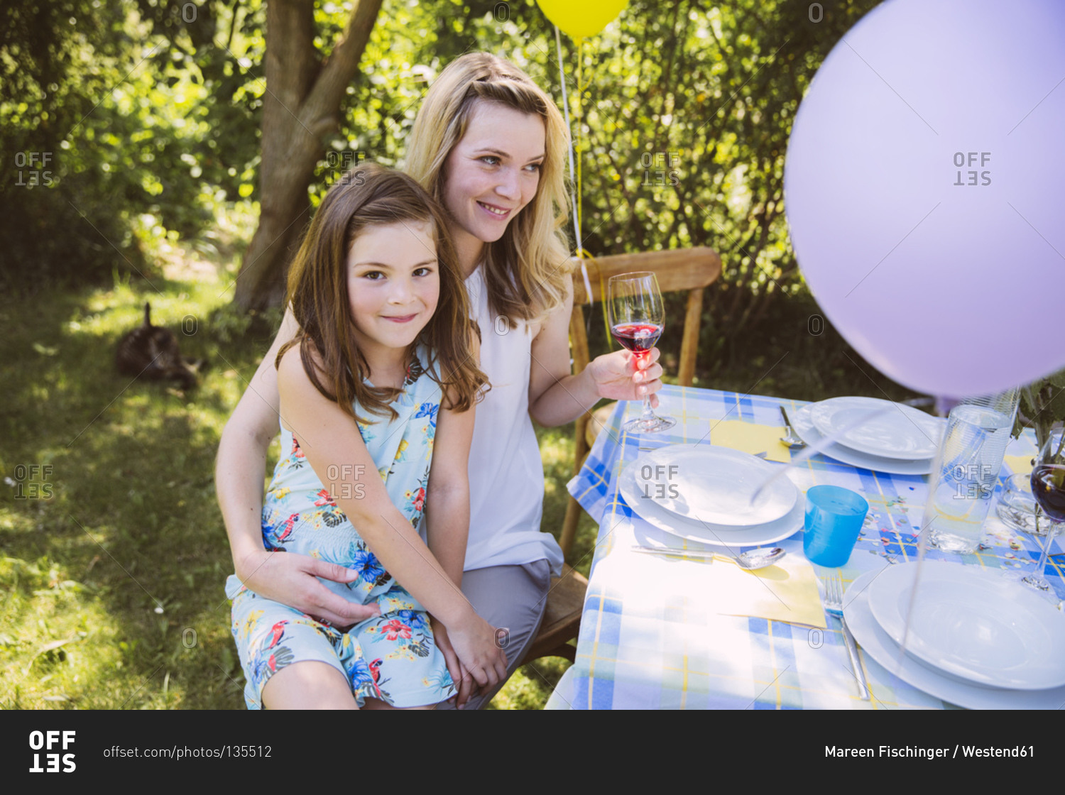 Daughter sitting on mother's lap at garden party table