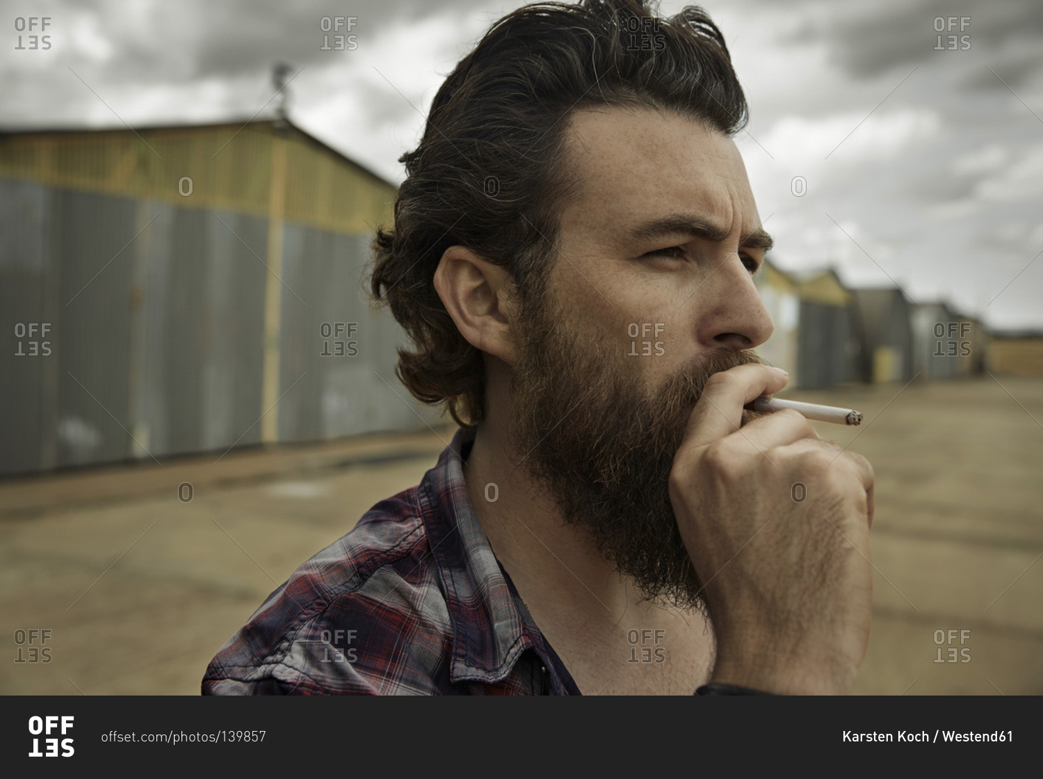 Man with full beard smoking cigarette stock photo - OFFSET