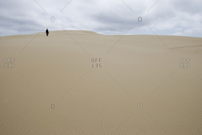 A woman walking alone on a sand dune in the distance