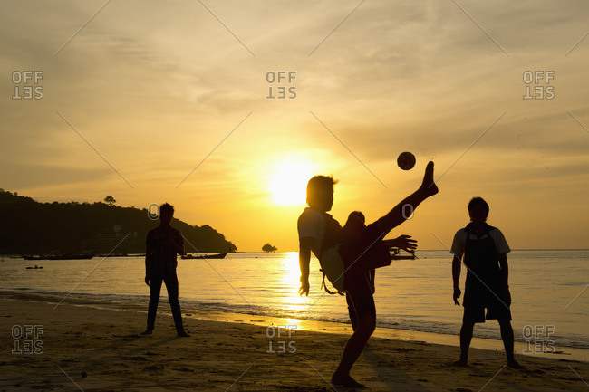Men playing takraw ball at sunset on the beach