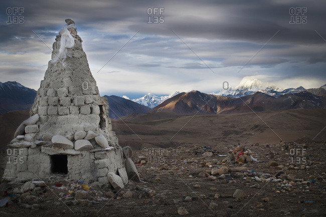 A stone conical structure on a barren landscape with mountains in the background, Tibet