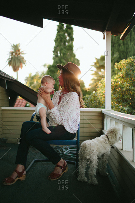 Woman holding a baby on a porch next to a watchful poodle
