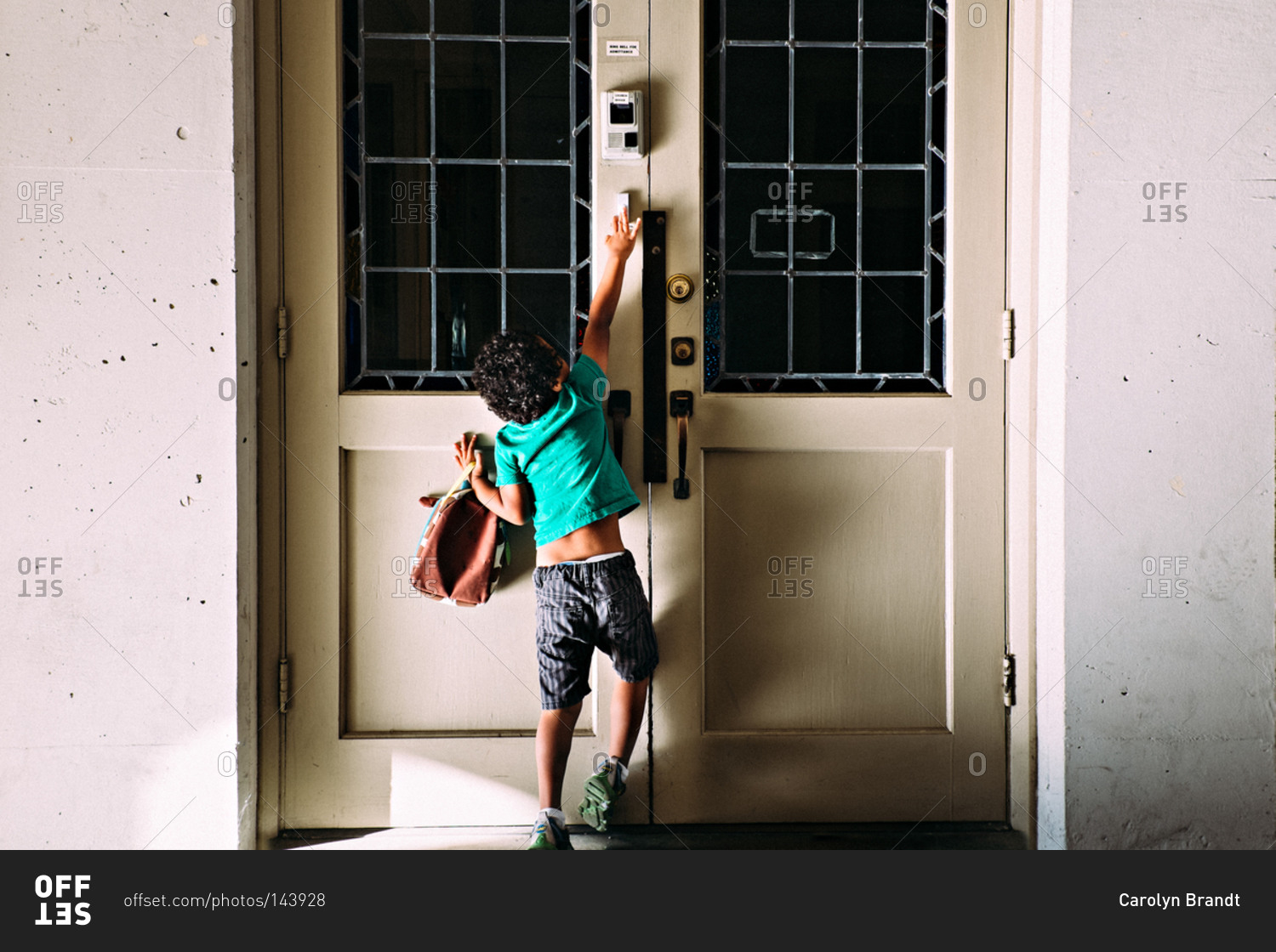 A boy reaches up to ring a doorbell