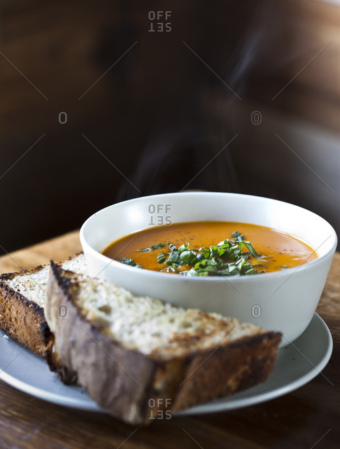 A bowl of soup sits next to two pieces of bread