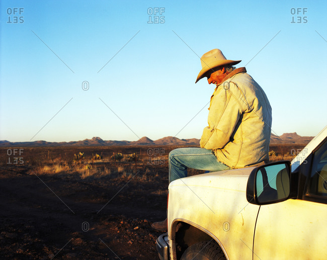 Cowboy sitting on truck hood stock photo - OFFSET