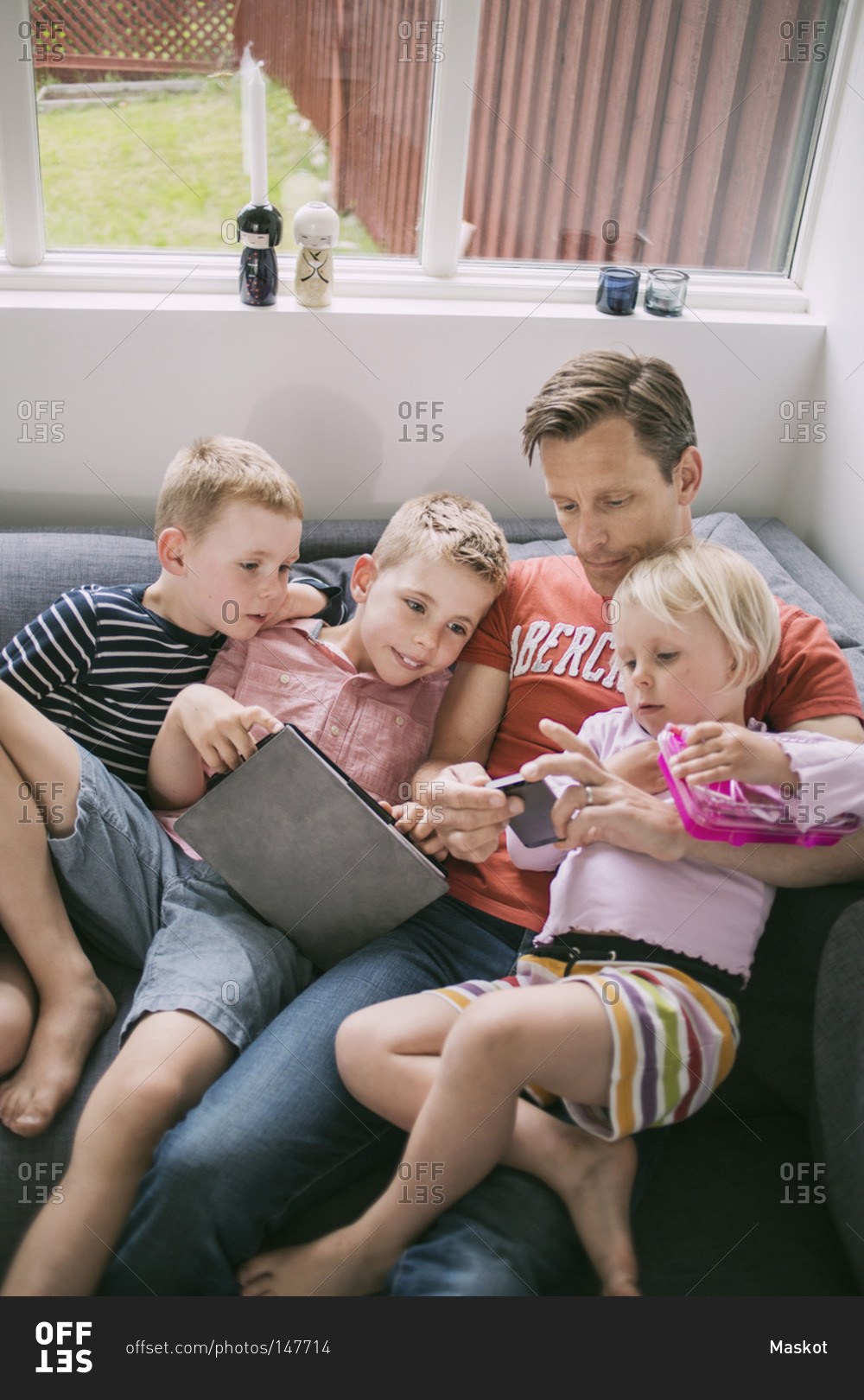 Father and children using technologies on sofa at home