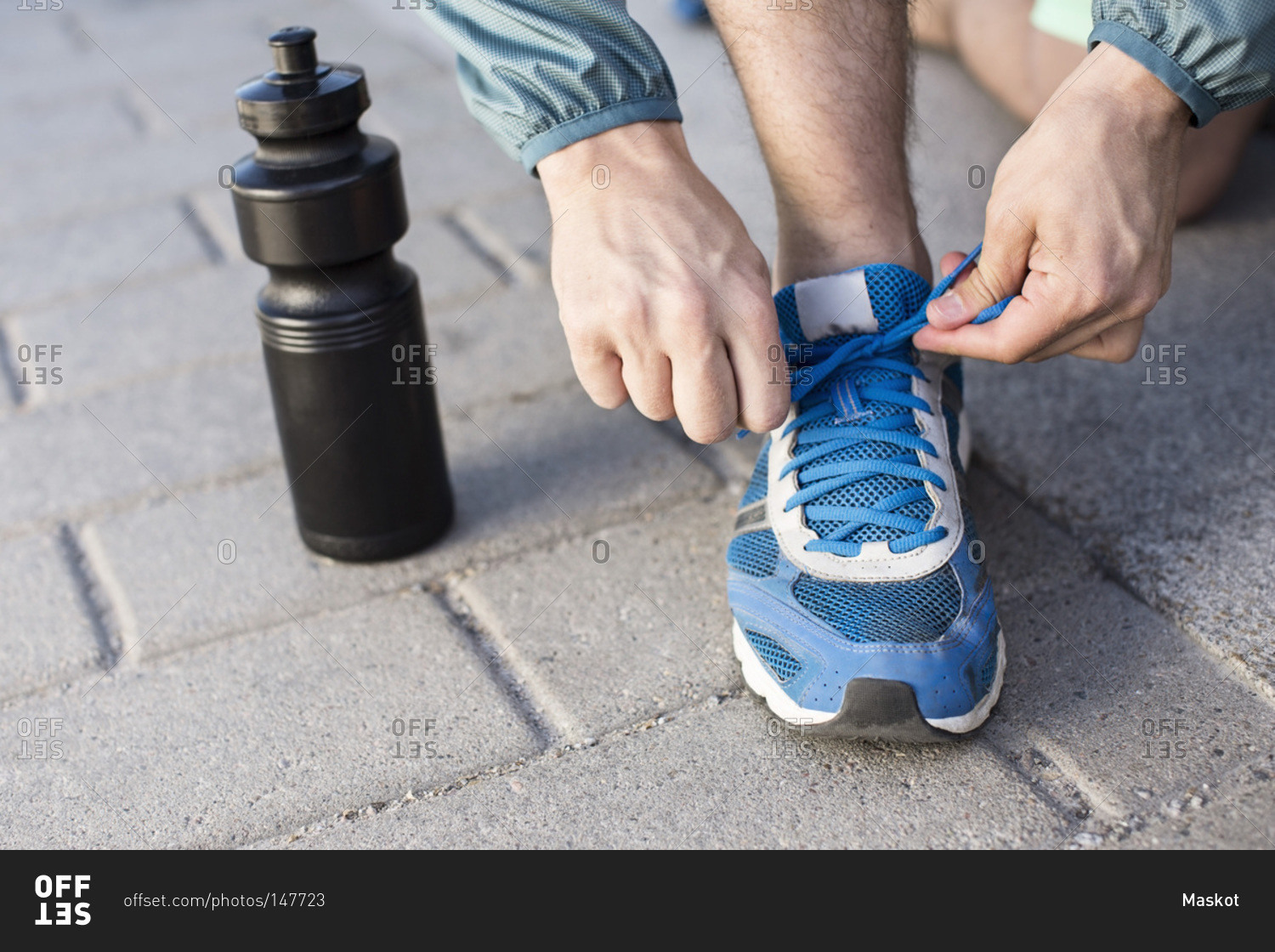 Low section of man tying sport shoelace by water bottle on street