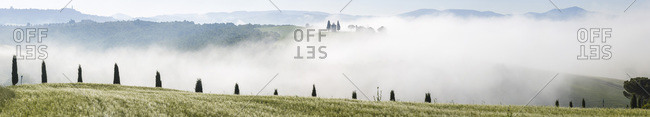 Heavy mist covering hills and chapel in Tuscany