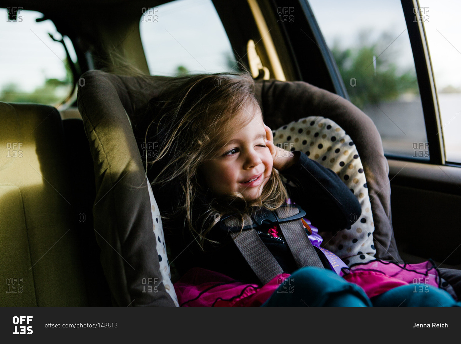 Girl in car seat squinting at sun
