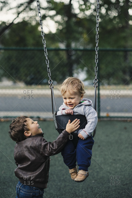 Little boy pushing baby brother on swing