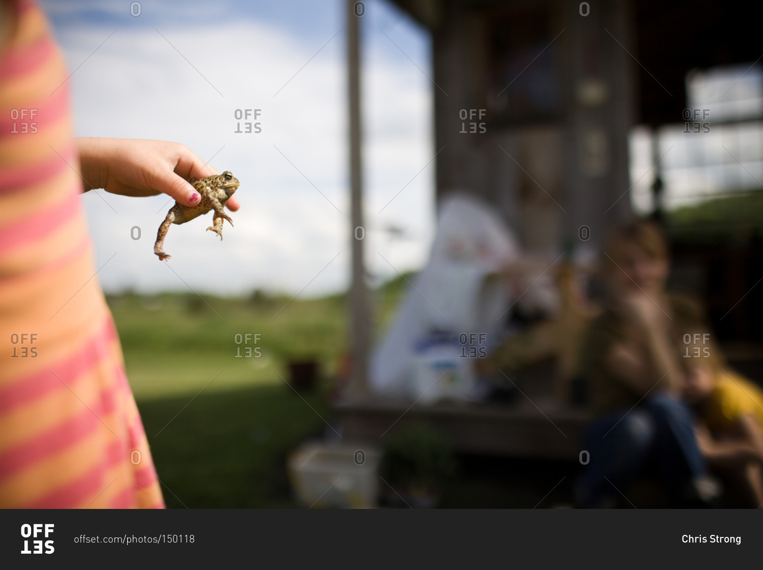 Girl holding a frog near rural house