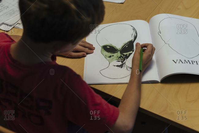 A boy coloring an alien at a table