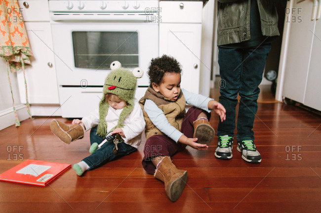 Two toddlers sitting on wooden floor trying to best and comfortable toddler shoes for all kinds of occasions