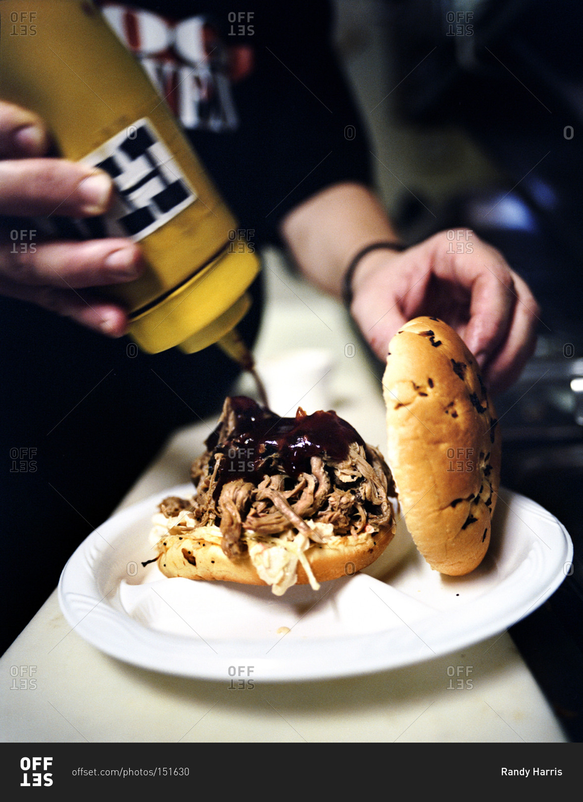 Person adding special hog heaven sauce to a pulled pork sandwich