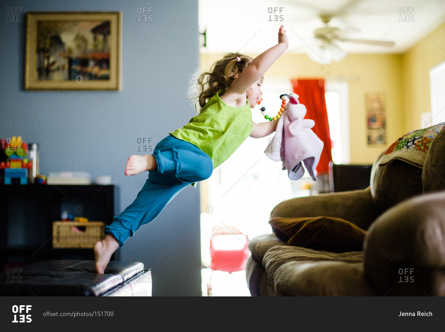 Young girl jumping over to a couch stock photo OFFSET