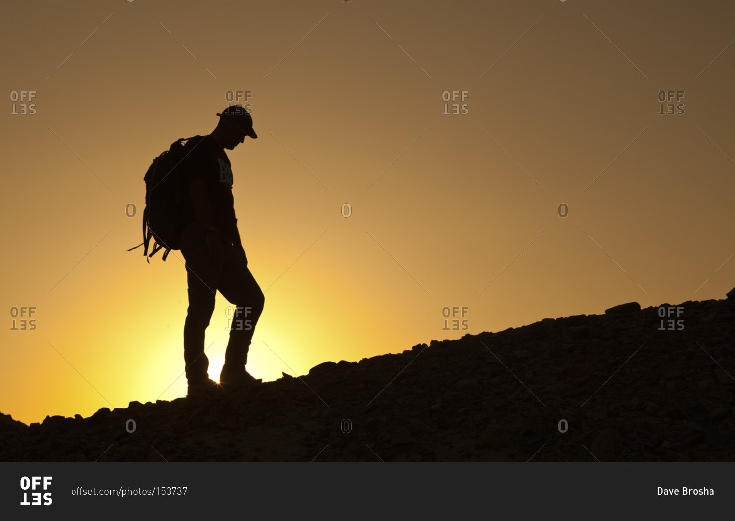 Hiker on hill backlit by orange sunset