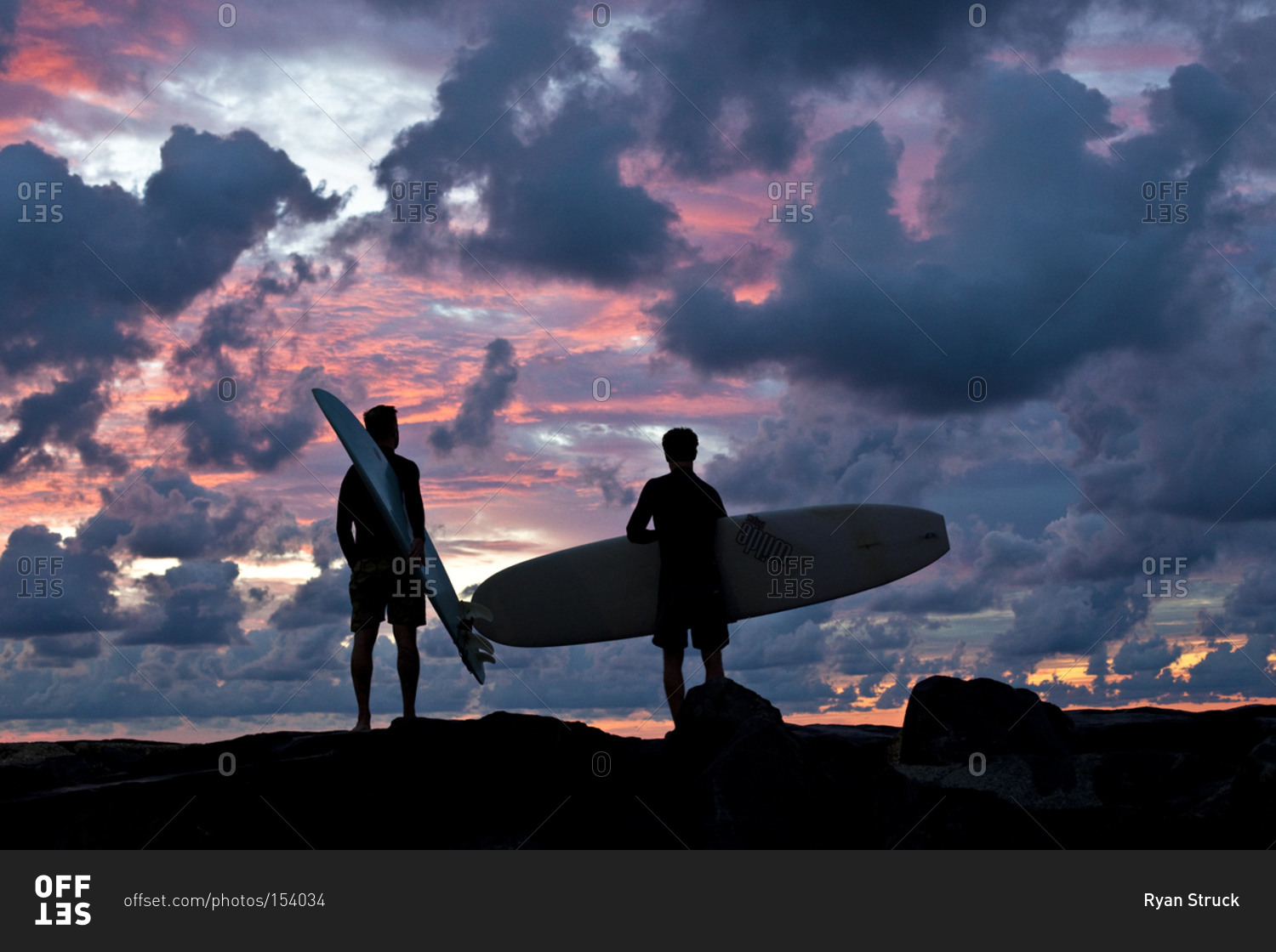 Two men with surfboards backlit by sunset