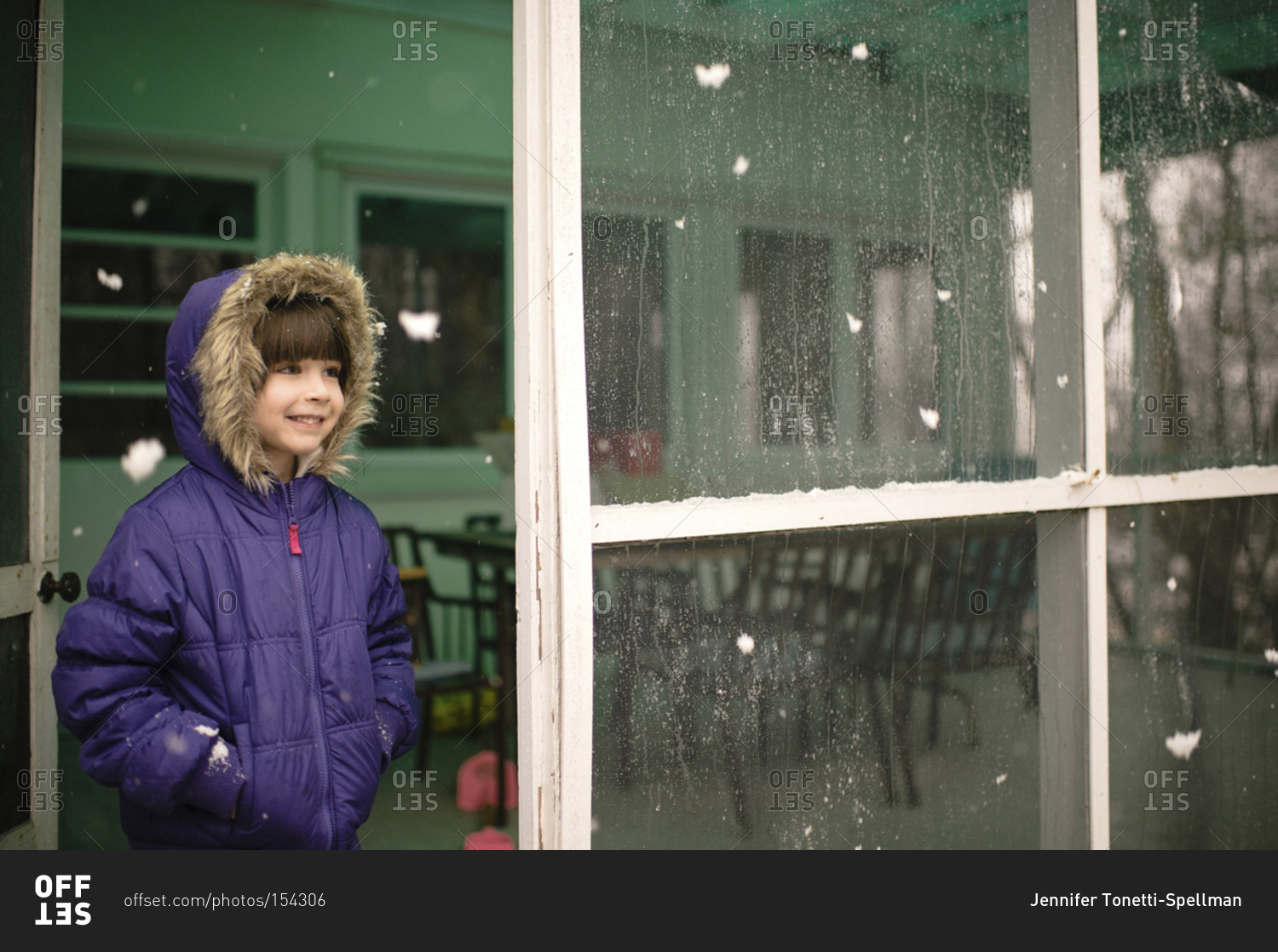 A little girl on screen porch watching snow