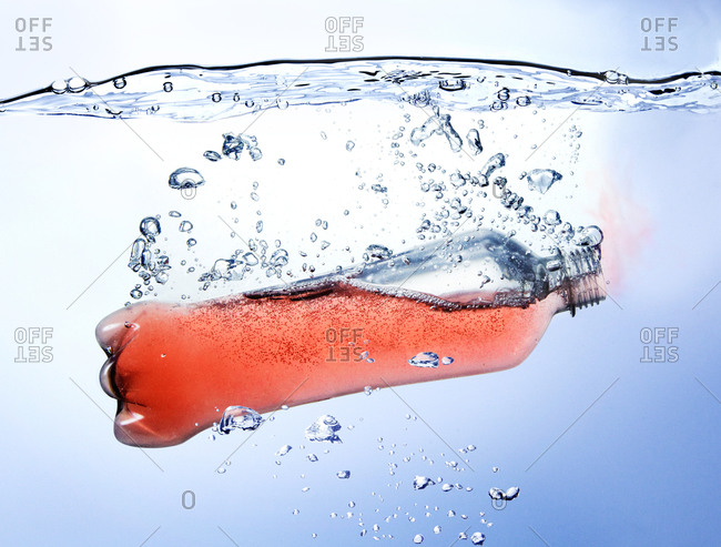 Bottle of red carbonated fruit beverage falling into water